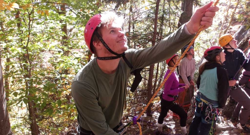 A person wearing a helmet looks up as they belay an unseen rock climber above. 